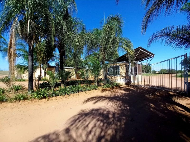 Front entrance view of the property featuring a metal security gate, perimeter wall, and a small guard house structure.