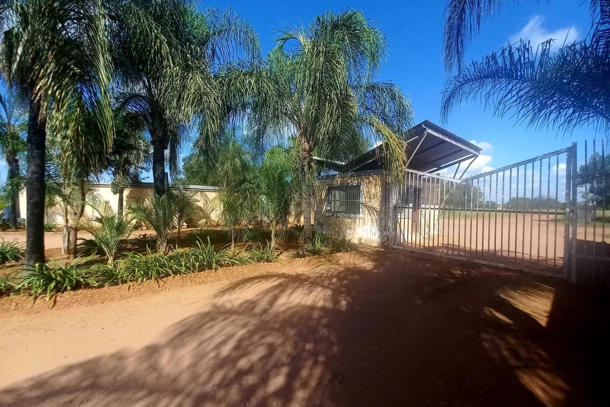 Front entrance view of the property featuring a metal security gate, guard house, and established palm tree landscaping.