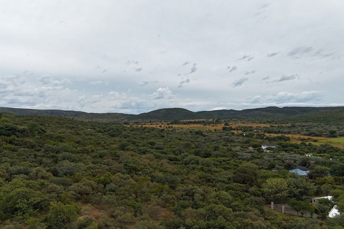 An expansive aerial view of the natural landscape, showcasing rolling hills and dense indigenous vegetation surrounding the residential area.