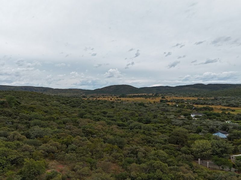 An expansive aerial view of the natural landscape, showcasing rolling hills and dense indigenous vegetation surrounding the residential area.