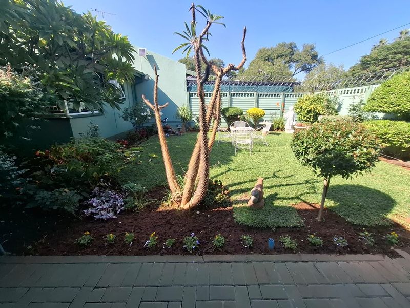 A well-maintained rear garden featuring a paved patio area, manicured lawn, established landscaping, and secure perimeter fencing with razor wire.