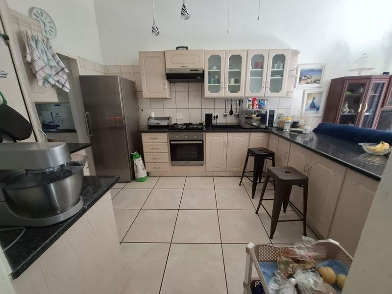 A functional kitchen featuring light-toned cabinetry, dark granite countertops, a gas hob, built-in oven, and tiled flooring with a breakfast bar area.