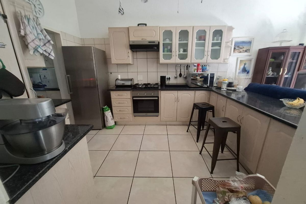 A functional kitchen featuring light-toned cabinetry, dark granite countertops, a gas hob, built-in oven, and tiled flooring with a breakfast bar area.