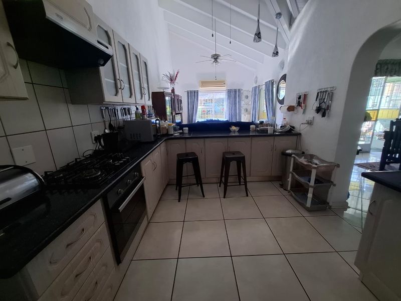 Open-plan kitchen featuring built-in cabinetry, gas hob, oven, and breakfast counter, set under a high vaulted ceiling with tiled flooring throughout.