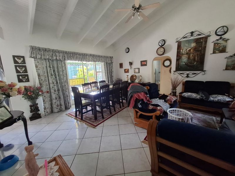 Spacious open-plan living and dining area featuring vaulted ceilings with exposed beams, ceramic tile flooring, and direct access to the outdoor patio.
