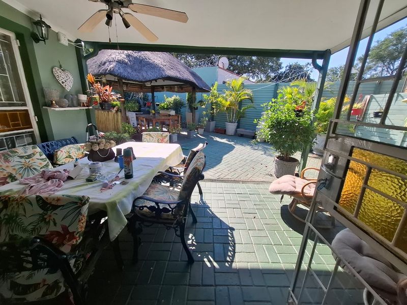 A covered outdoor patio area featuring paved flooring, a ceiling fan, and a view of the rear garden with a thatched lapa.