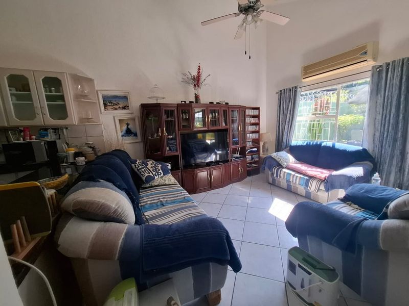 Open-plan living area featuring tiled floors, high ceilings with a fan, and a wall-mounted air conditioning unit with access to the garden.