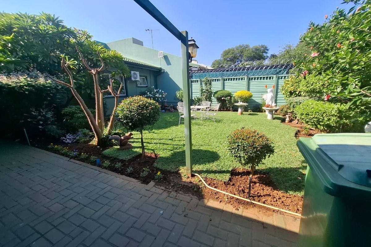 A well-maintained rear garden featuring a paved patio area, manicured lawn, and secure perimeter fencing.