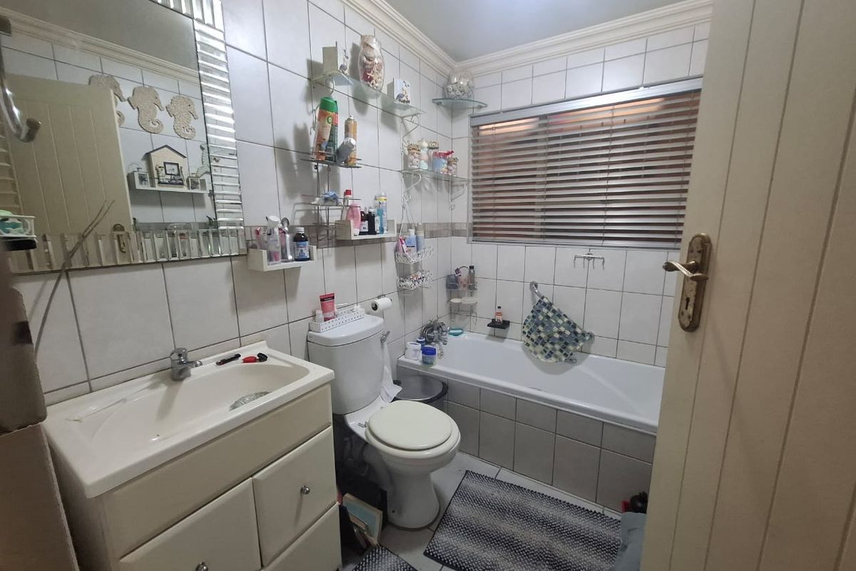 A functional bathroom featuring a vanity cabinet, bathtub, toilet, and full-height wall tiling, providing a practical layout for daily use.