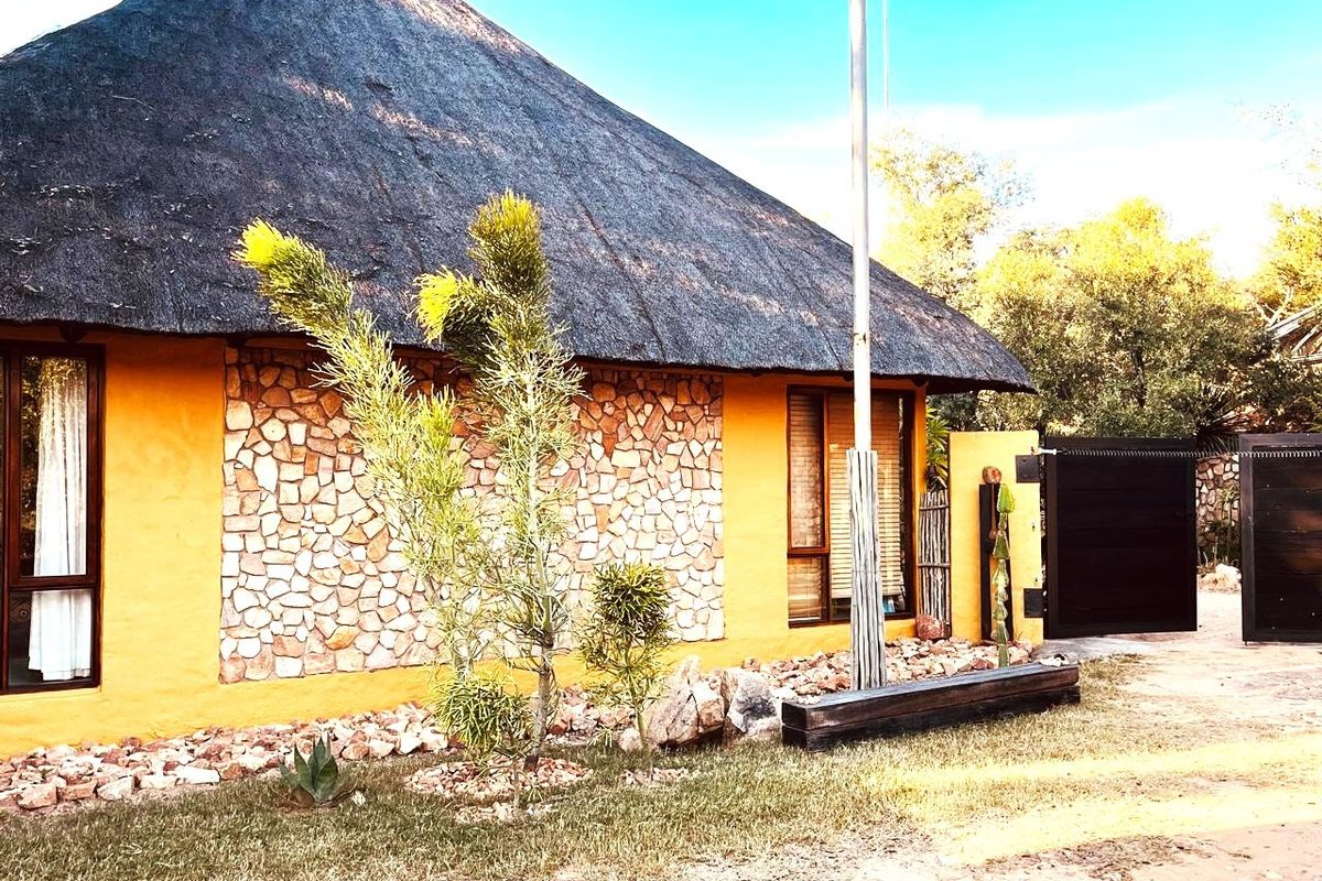 Front elevation of a house featuring a traditional thatch roof, stone cladding accents, and a secure gated entrance.