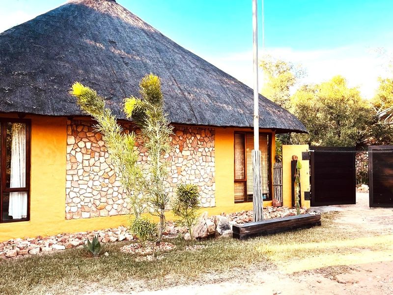 Front elevation of a house featuring a traditional thatch roof, stone cladding accents, and a secure gated entrance.