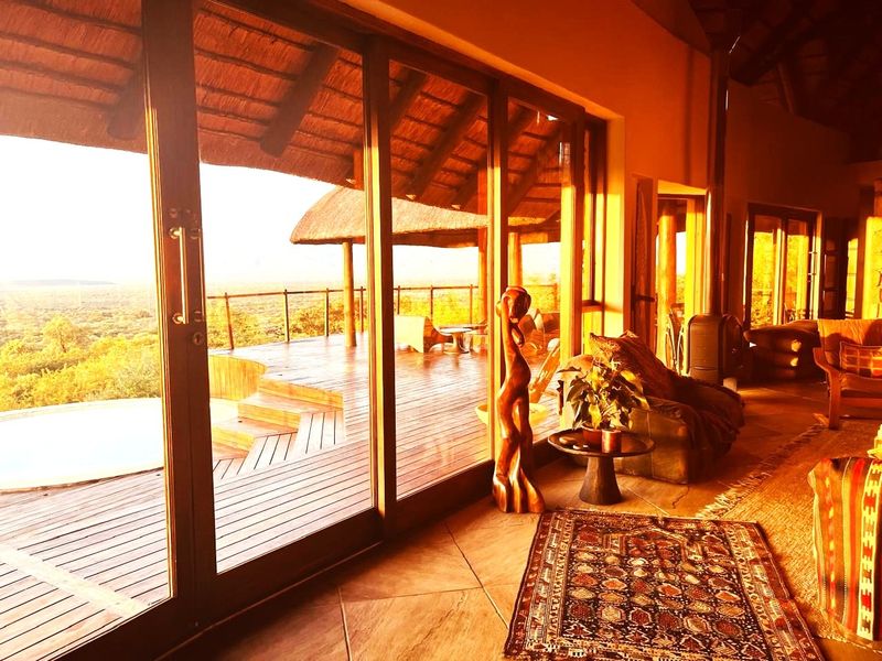 Spacious living area featuring large sliding glass doors that open onto a wooden deck with scenic views, complemented by a thatch roof and fireplace.