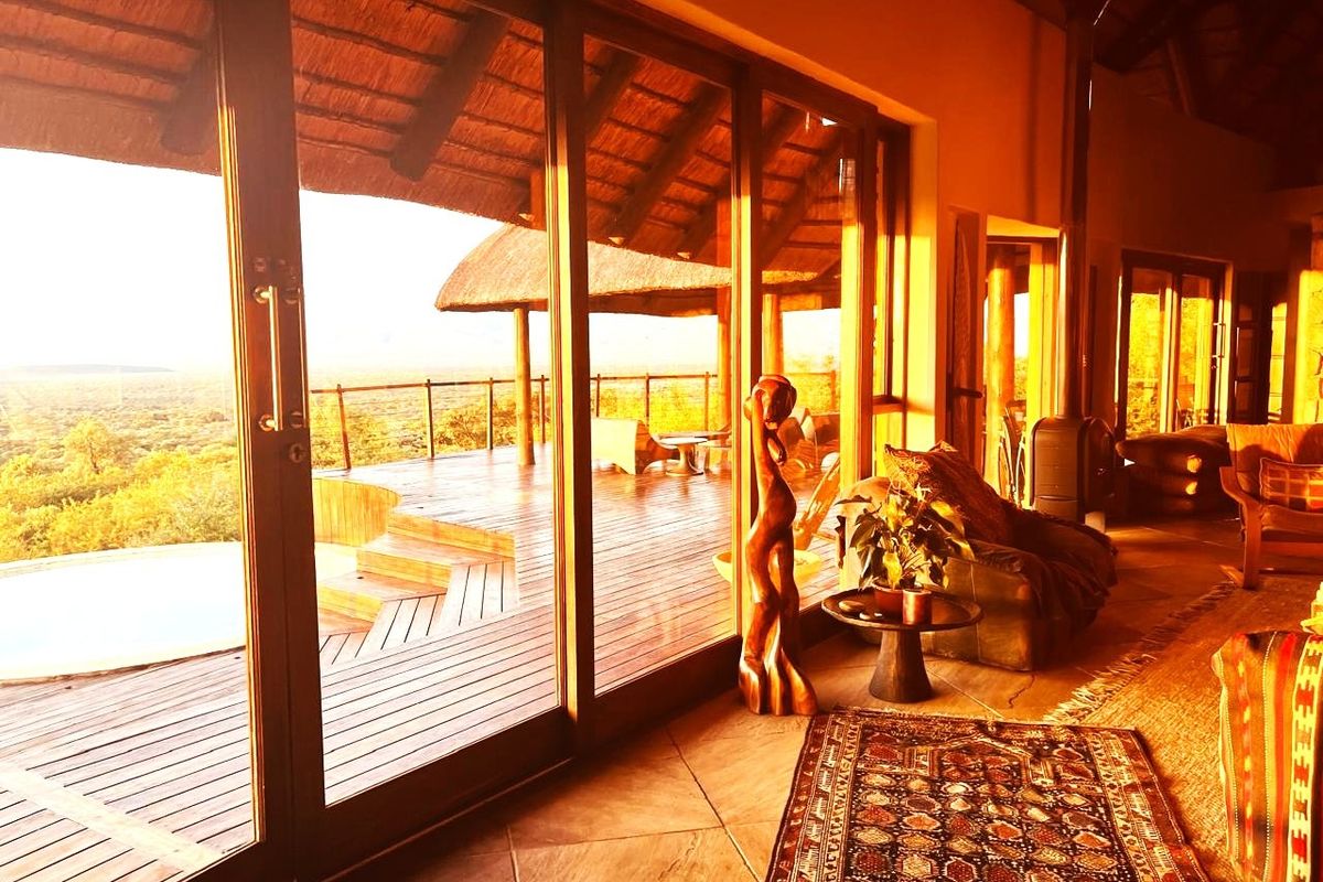 Spacious living area featuring large sliding glass doors that open onto a wooden deck with scenic views, complemented by a thatch roof and fireplace.