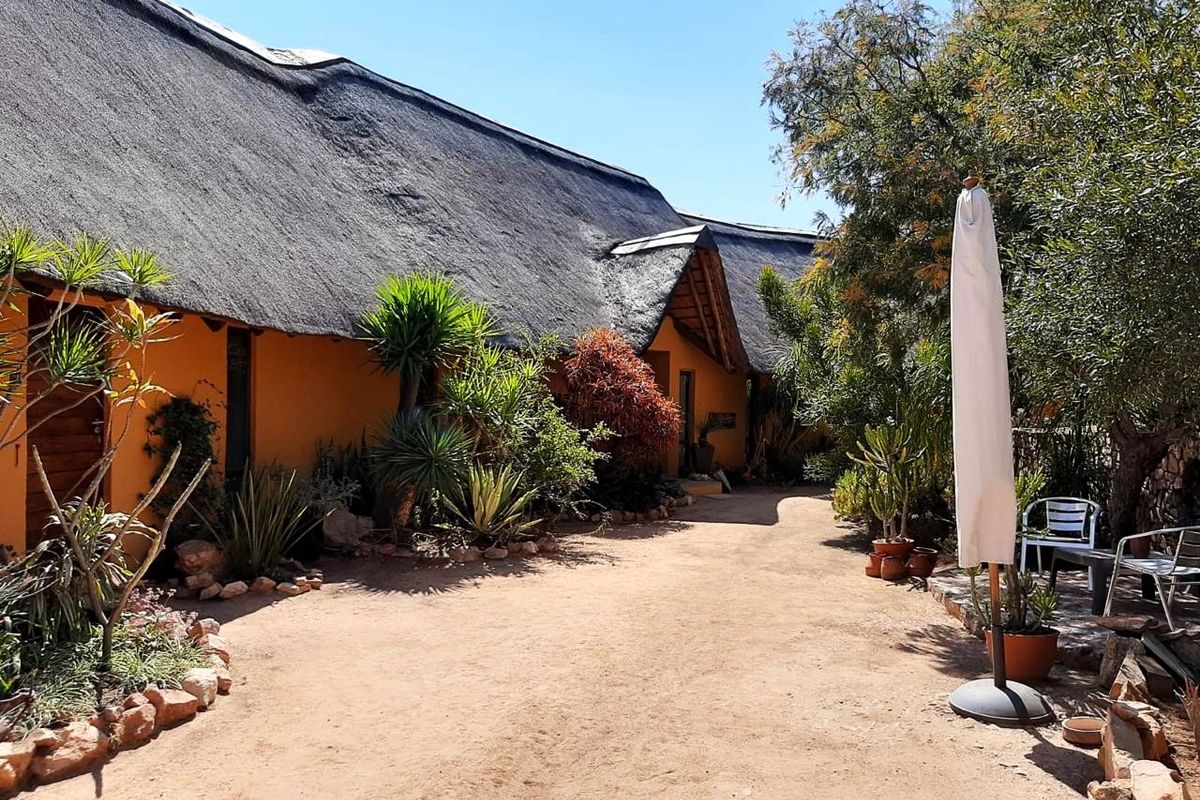 A well-maintained rear exterior view featuring a traditional thatched roof, warm-toned stucco walls, and a landscaped garden area with stone borders.