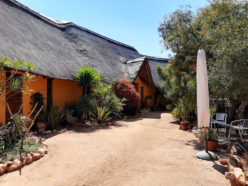 A well-maintained rear exterior view featuring a traditional thatched roof, warm-toned stucco walls, and a landscaped garden area with stone borders.
