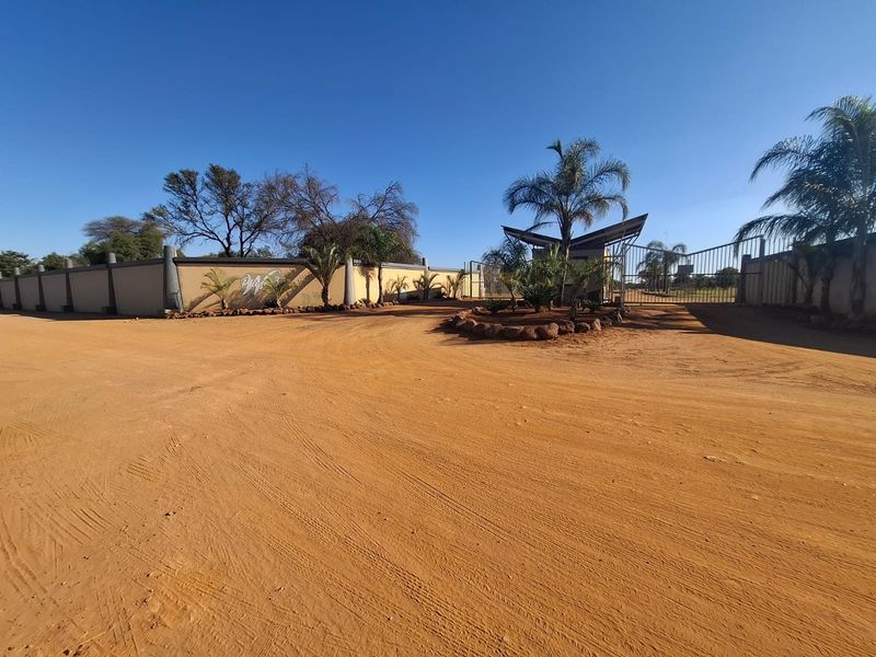 Entrance view of the residential property featuring a perimeter wall, gated access, and a natural dirt driveway.