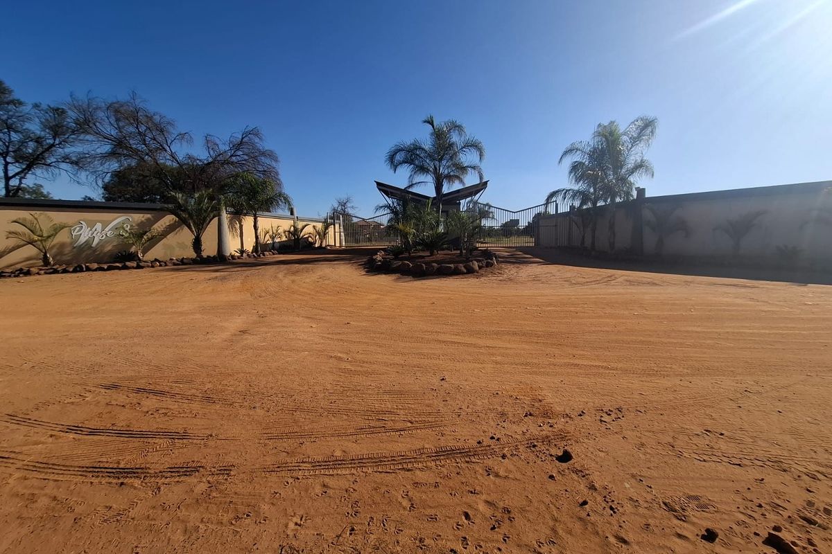 Entrance view of a residential estate featuring a gated access point, perimeter walling, and established landscaping.