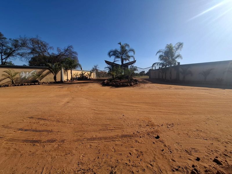 Entrance view of a residential estate featuring a gated access point, perimeter walling, and established landscaping.