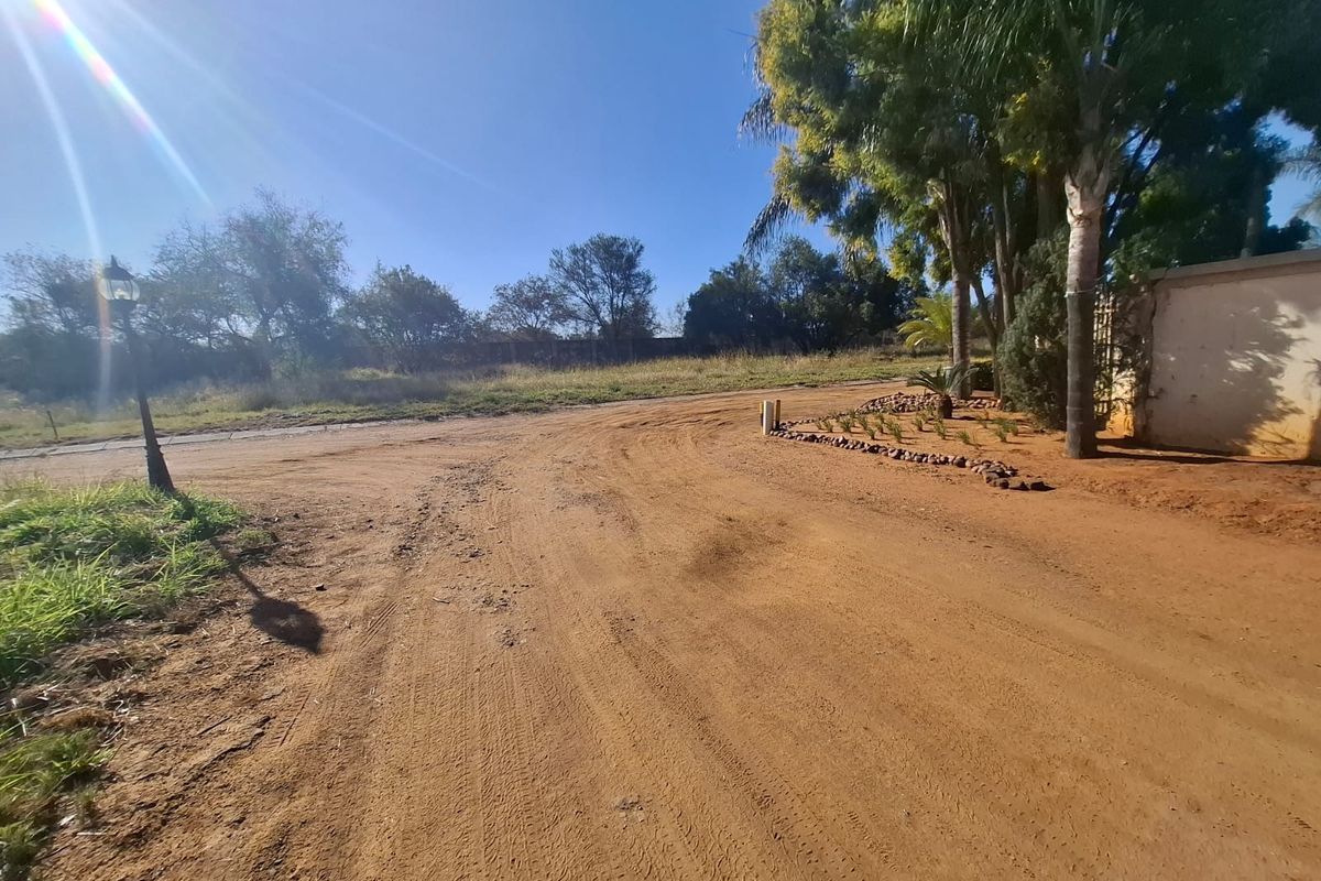 A view of the unpaved access road and entrance area of the vacant residential property, featuring mature trees and perimeter walling.