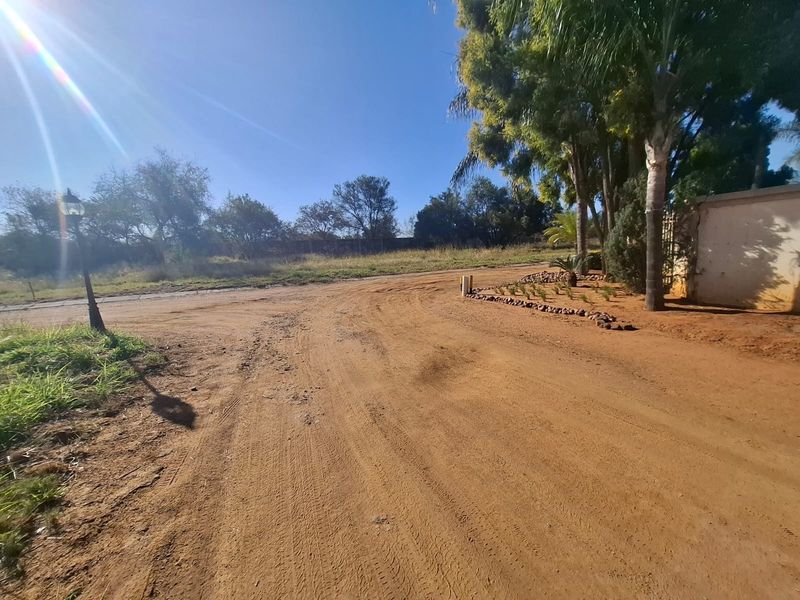 A view of the unpaved access road and entrance area of the vacant residential property, featuring mature trees and perimeter walling.