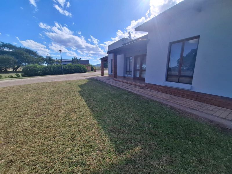 Rear view of the townhouse featuring a covered patio, brick paving, and a well-maintained lawn area.