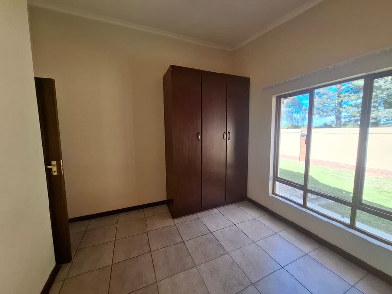 A bright, empty bedroom featuring tiled flooring, a built-in wooden wardrobe, and a large window providing natural light.
