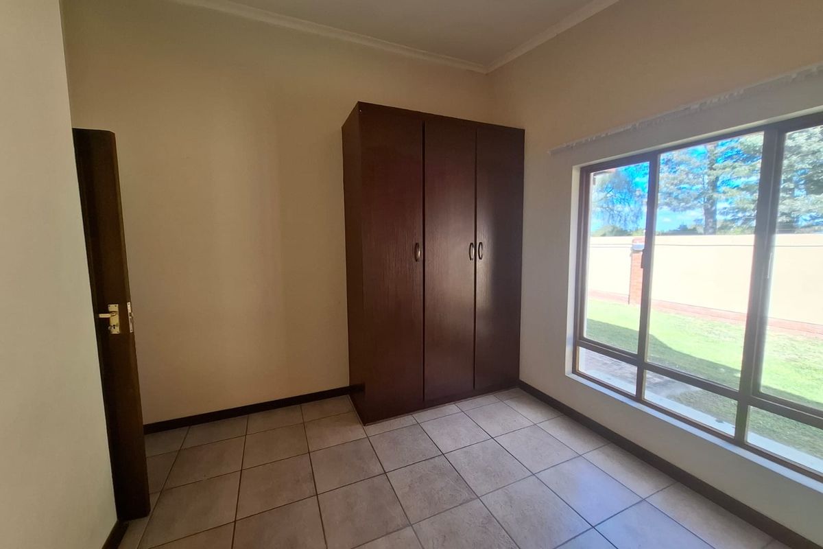 A bright, empty bedroom featuring tiled flooring, a built-in wooden wardrobe, and a large window providing natural light.