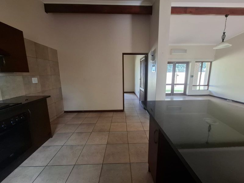 Spacious open-plan kitchen and living area featuring dark cabinetry, granite countertops, tiled flooring, and exposed timber beams, leading to a bright outdoor access point.