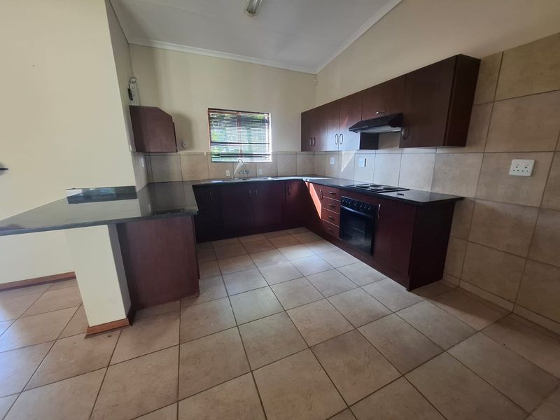 A functional kitchen featuring dark wood cabinetry, granite countertops, built-in oven, electric hob, and tiled flooring, offering a clean and practical workspace.