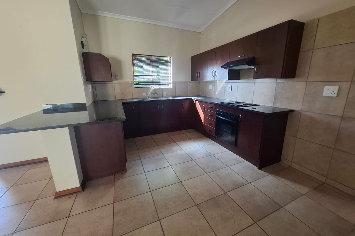 A functional kitchen featuring dark wood cabinetry, granite countertops, built-in oven, electric hob, and tiled flooring, offering a clean and practical workspace.