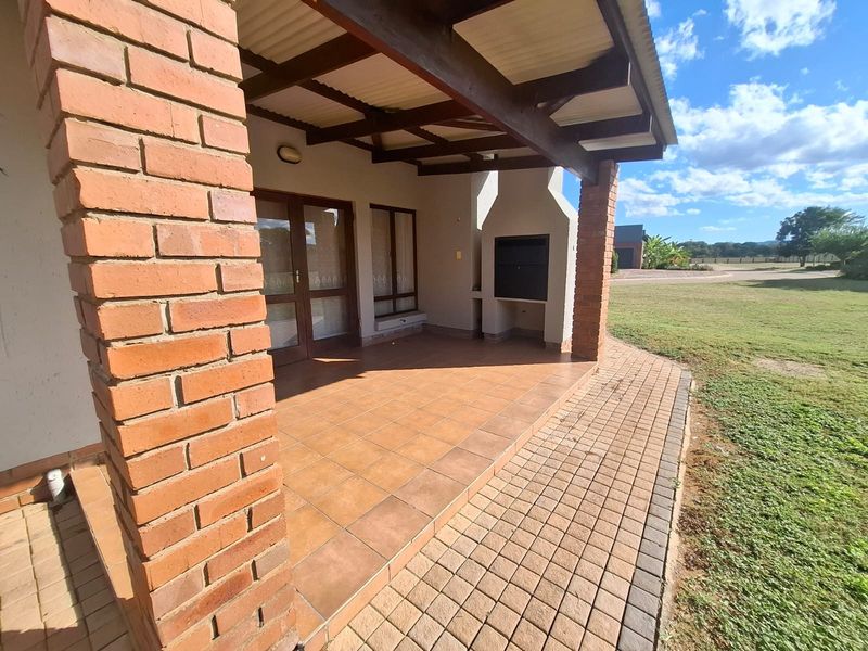 Covered patio featuring a built-in braai, brick pillars, and tiled flooring, overlooking a spacious garden area.