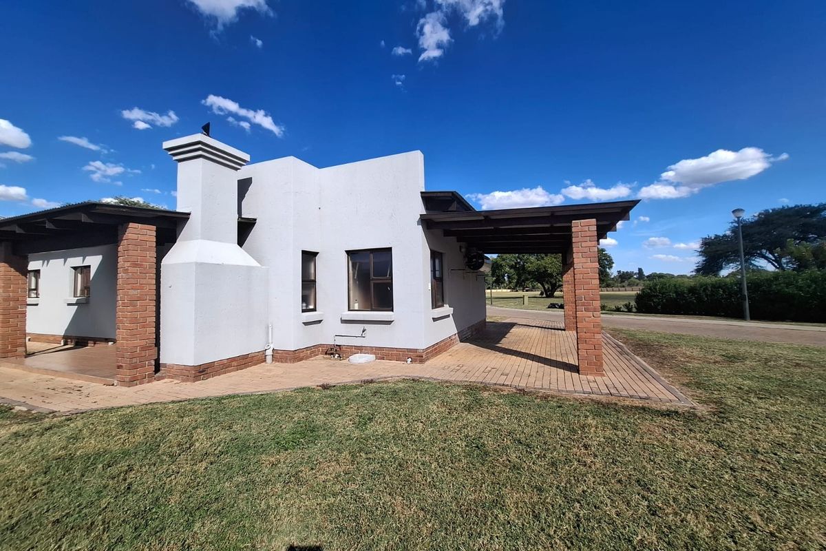 Rear view of the townhouse featuring a covered patio area with brick pillars, a prominent chimney, and paved outdoor flooring.