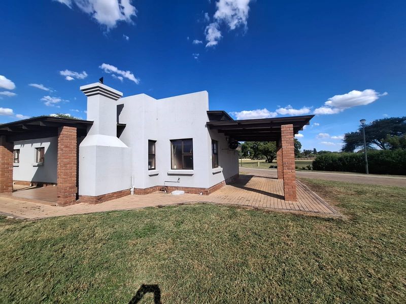 Rear view of the townhouse featuring a covered patio area with brick pillars, a prominent chimney, and paved outdoor flooring.