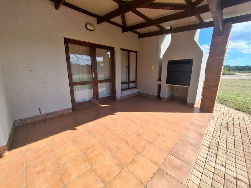 Covered patio featuring a built-in braai, tiled flooring, and direct access to the garden through double glass doors.