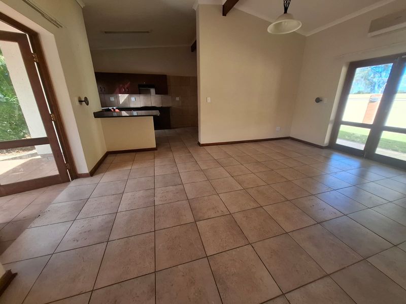 Spacious open-plan living area featuring ceramic floor tiles, exposed ceiling beams, and direct access to outdoor spaces, adjacent to a functional kitchen.