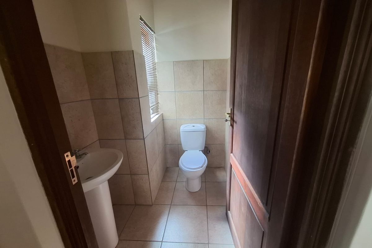 A functional guest bathroom featuring a pedestal basin, toilet, and neutral wall and floor tiling.