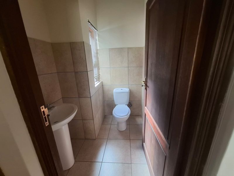 A functional guest bathroom featuring a pedestal basin, toilet, and neutral wall and floor tiling.