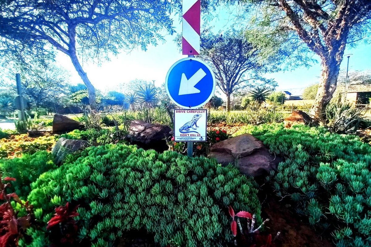 A well-maintained landscaped garden area featuring mature trees, shrubs, and traffic signage at the property entrance.
