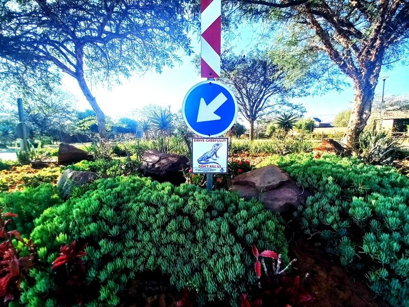 A well-maintained landscaped garden area featuring mature trees, shrubs, and traffic signage at the property entrance.
