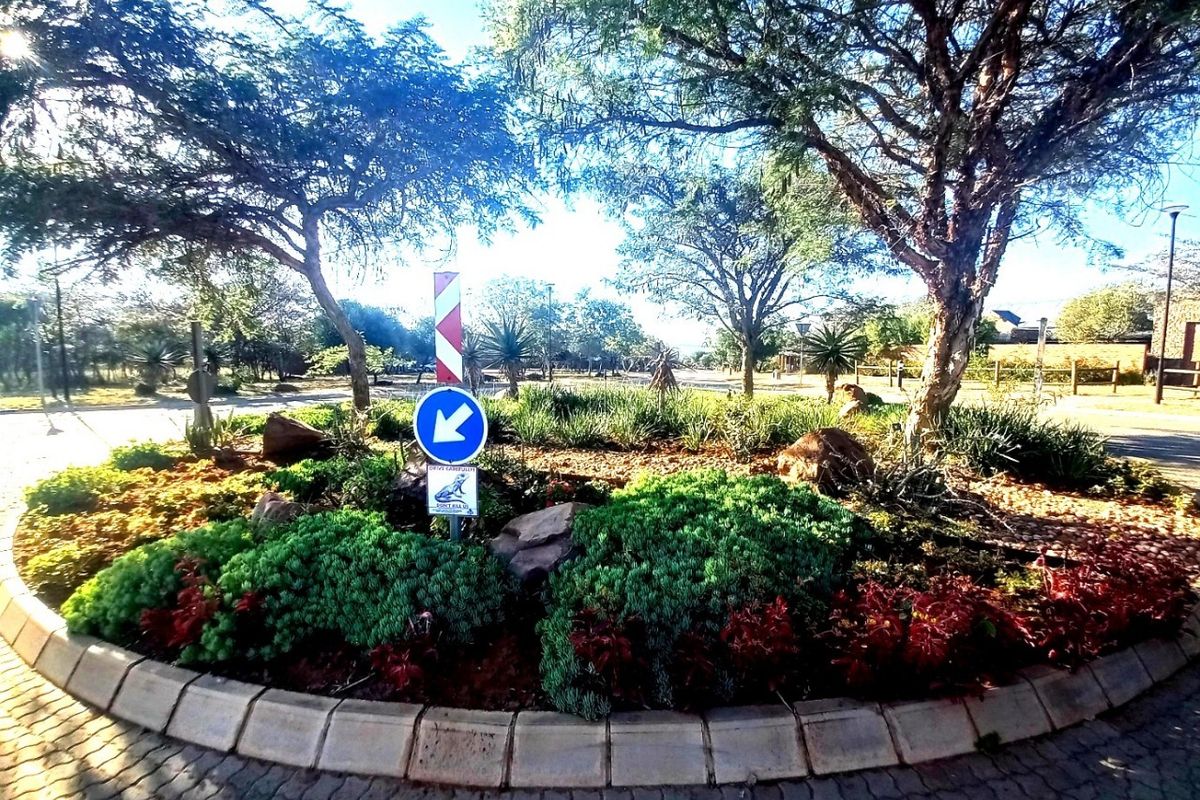 A well-maintained landscaped roundabout featuring mature trees, shrubs, and paved curbing within the residential estate.