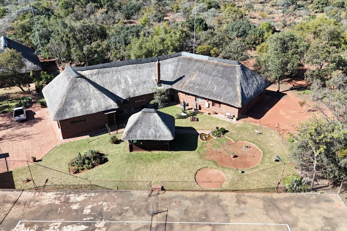 Aerial view of a farm property featuring a large thatch-roofed residence, a detached gazebo, paved driveway, and a private tennis court set within a natural landscape.