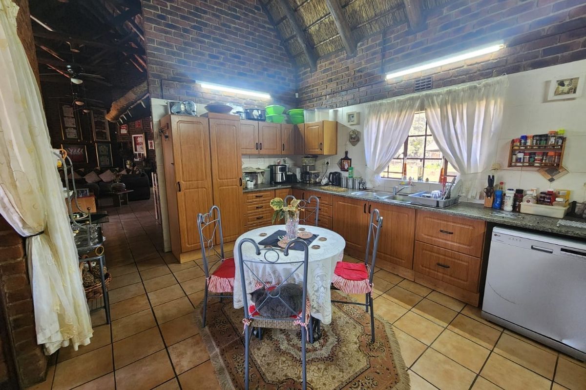 A rustic kitchen featuring exposed brick walls, a high thatched ceiling, wooden cabinetry, granite countertops, and ceramic tiled flooring.