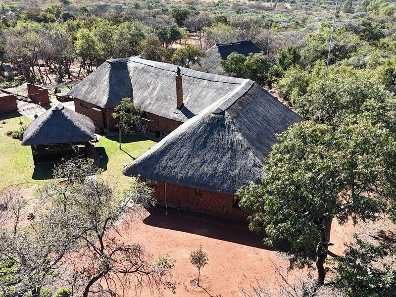 Aerial view of a farm property featuring multiple buildings with traditional thatched roofs, brick construction, and surrounding natural landscape.