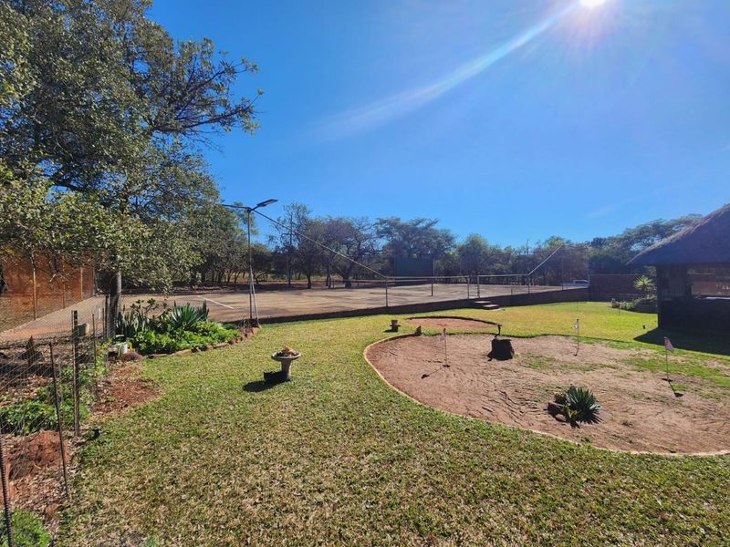 Outdoor recreational area featuring a tennis court with floodlights and a small putting green set within a landscaped garden.