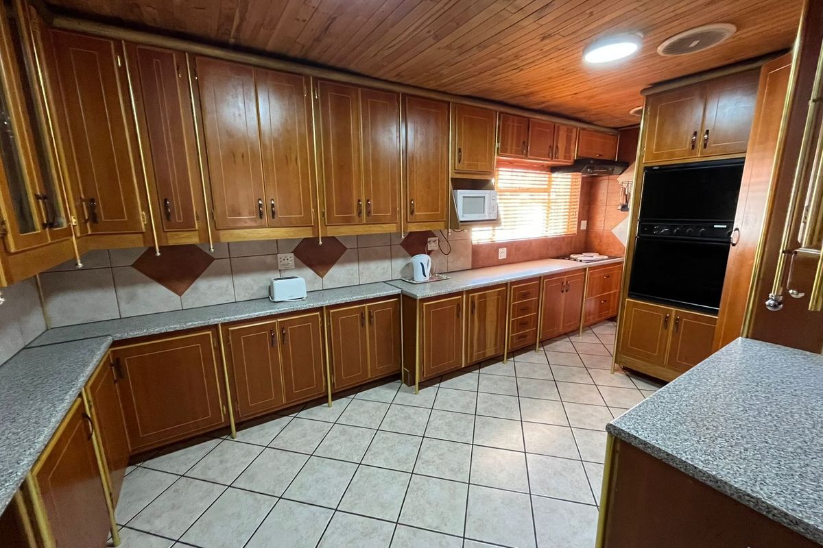 A functional kitchen featuring extensive wooden cabinetry, laminate countertops, a built-in double oven, and a timber-clad ceiling with tiled flooring.