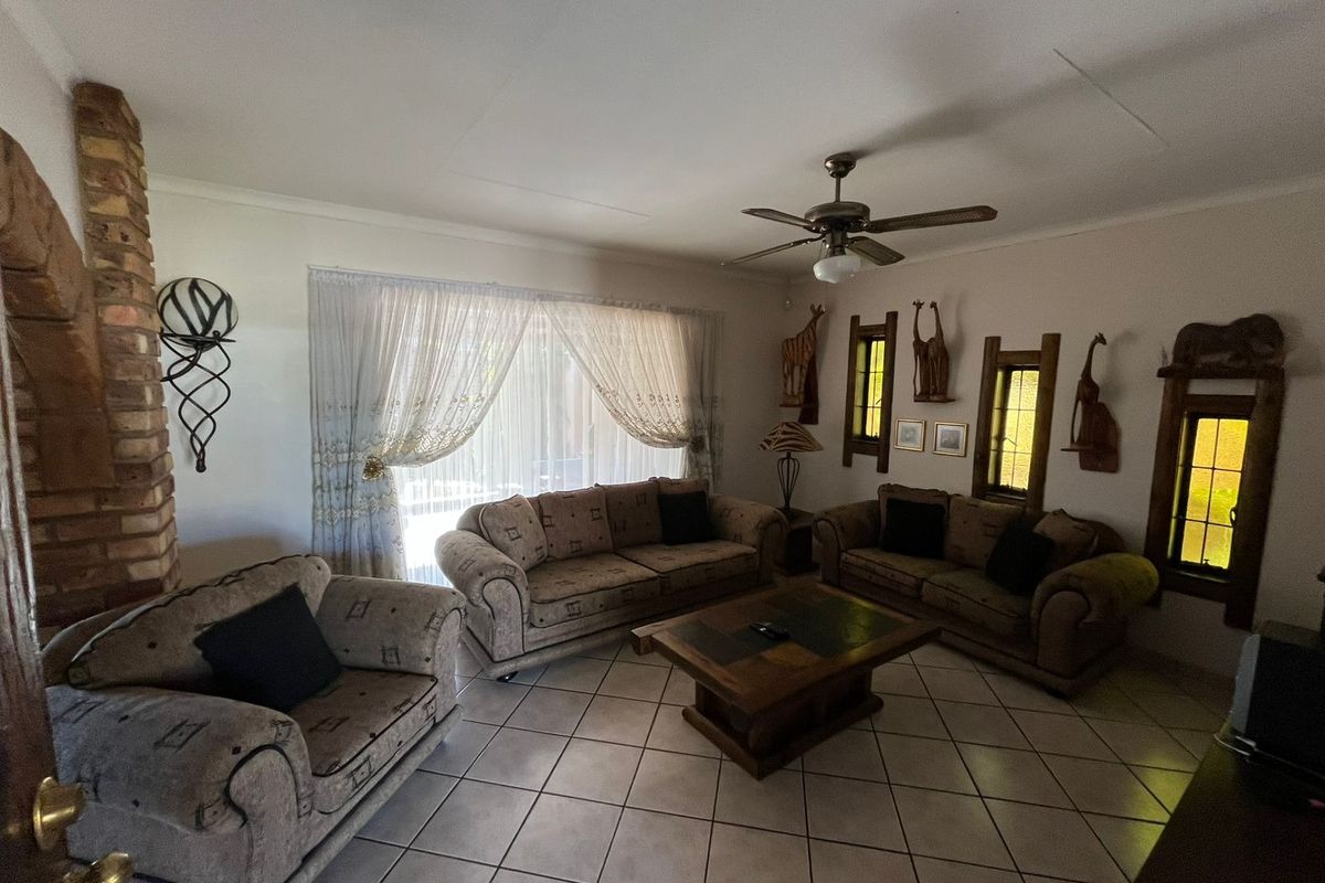 A living room featuring tiled flooring, a brick fireplace, and a ceiling fan, with natural light entering through large windows.