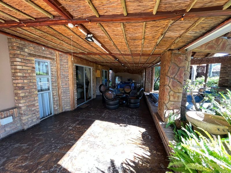 A covered patio area featuring a rustic thatched roof, exposed brickwork, stone-clad pillars, and tiled flooring, providing a sheltered outdoor entertainment space.