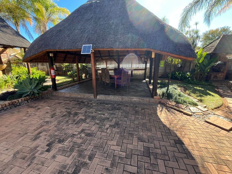 A covered outdoor patio area featuring a traditional thatch roof, timber support posts, and paved flooring, ideal for outdoor entertaining.