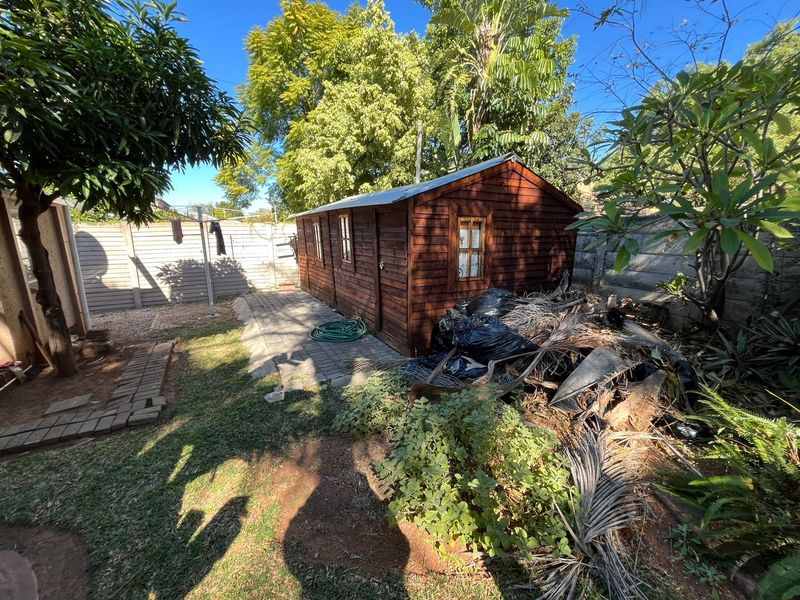 Rear garden area featuring a timber storage shed, paved pathway, and precast concrete boundary walling.