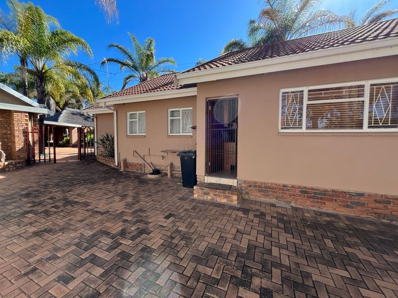 Rear exterior view of the house featuring brick paving, a tiled roof, and secure access points with security gates and bars.